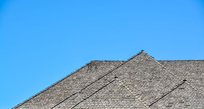 Massive roofs of residential house on blue sky background. Family house with big roofs tiled by wooden shingles