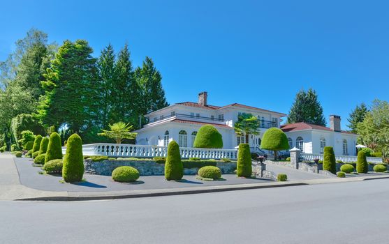 Luxury residential house fenced with white balustrade on the top of terrace decorated with topiary trees and plants