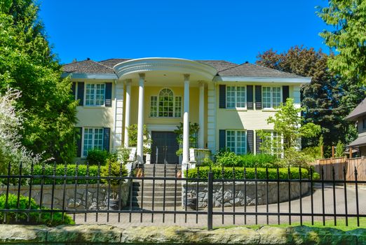 Luxury residential house with metal fence in front in suburb of Vancouver. Beautiful house with green lawn in front on blue sky background