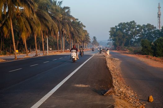 Morning Road Amidst Trees with motorcyclists, Goa, India