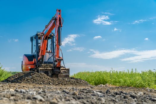 A small excavator is building a new road on a green field