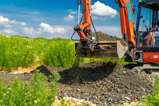 A small excavator is building a new road on a green field