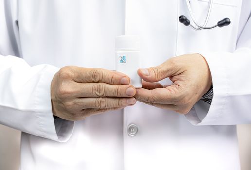 A male doctor holding a white medicine bottle.