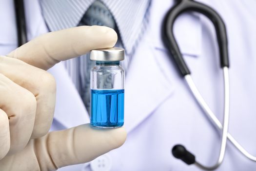 A doctor in white coat holding a medicine vial containing blue liquid. Vaccine, concept fight agaist virus coivid-19.