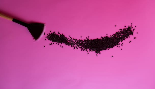 cosmetic brush sweeps black sesame seeds from a pink background. High quality photo