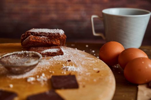 Chocolate cakes stacked on a wooden table. next to it are eggs and pieces of chocolate. blurred background. High quality photo