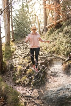 Active sporty woman listening to the music while running in autumn fall forest. Female runner training outdoor. Healthy lifestyle image of young caucasian woman jogging outside.