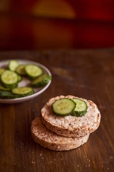 round buckwheat bread on which are two fresh cucumbers on a brown background. High quality photo