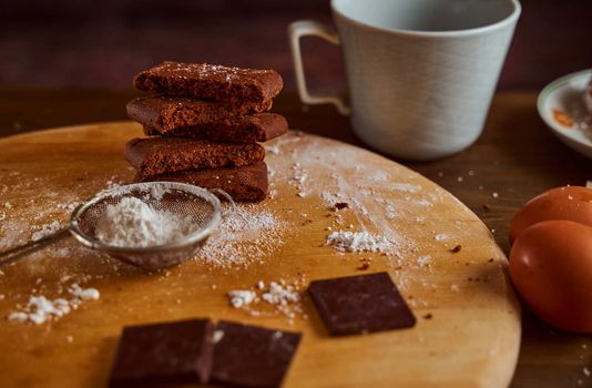 Chocolate cakes stacked on a wooden table. next to it are eggs and pieces of chocolate. blurred background. High quality photo