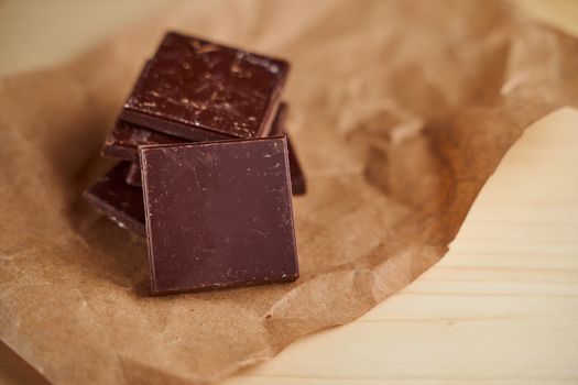 Pieces of chocolate bar lie on crafted brown paper. High quality photo