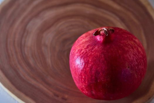 A red ripe pomegranate lies on a slice of a tree. Wooden background. High quality photo