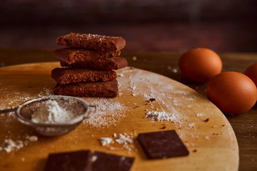 Chocolate cakes stacked on a wooden table. next to it are eggs and pieces of chocolate. blurred background. High quality photo