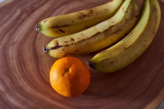 A yellow banana and orange mandarin lies on a slice of a tree. Wooden background. High quality photo