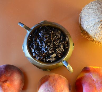 ingredients for dessert in the composition on the table: three ripe peaches, a copper jug with large leaf tea and a coconut