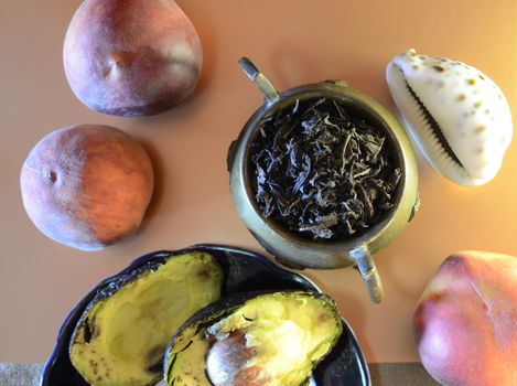 dessert in retro style: two halves of a ripe avocado on a plate, peaches, a copper jug with large leaf tea, coconut and seashell for composition