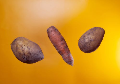 Not beautiful potatoes and carrots on an orange background. Isolate. High quality photo