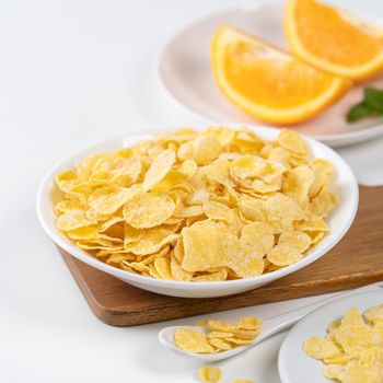 Corn flakes bowl sweeties with milk and orange on white background, close up, fresh and healthy breakfast design concept.