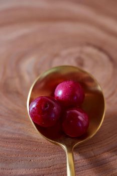 Ripe cherry berry on a wooden slice of wood in golden spoon. High quality photo