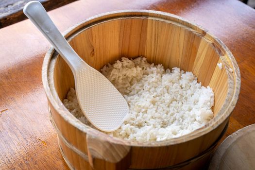 Delicious cooked plain rice in a big wooden bowl ready-to-eat with white rice spatula spoon at restaurant table, close up, lifestyle.