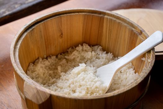 Delicious cooked plain rice in a big wooden bowl ready-to-eat with white rice spatula spoon at restaurant table, close up, lifestyle.