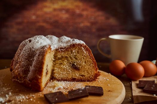 Cut homemade cupcake with chocolate cream inside with eggs and cup of tea on a wooden board. Black background. High quality photo