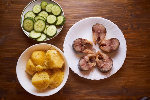 Boiled potatoes, cucumbers and sardines in plates on a brown table . High quality photo