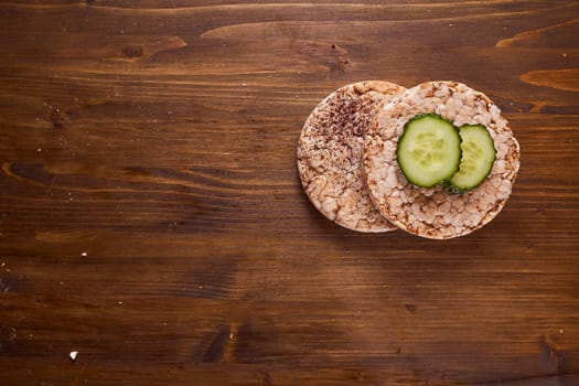 round buckwheat bread on which are two fresh cucumbers on a brown background. High quality photo