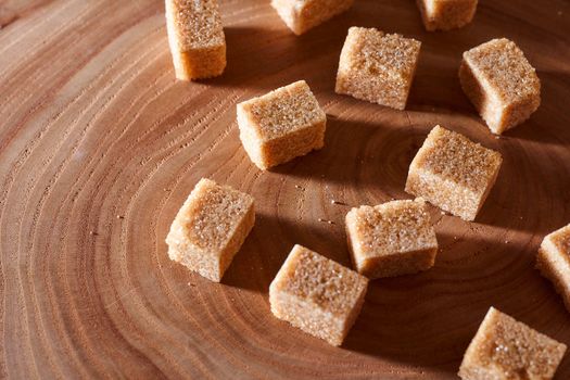 Brown cane sugar pieces on a slice, a plank of wood. High quality photo