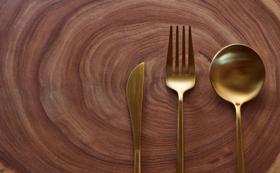 The golden knife, fork and spoon lies on a slice of a tree. wooden table. With copy space. High quality photo