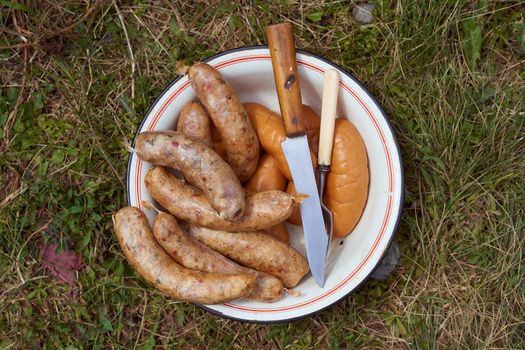 Homemade grilled meat sausages in a white plate on a green background. High quality photo