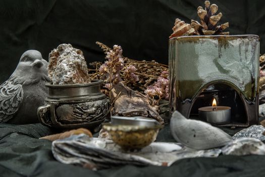 Beauty composition with Burning candle aroma oil lamp and Dry flower petals and Pine cones, Natural pine wood disc, Stones and Shells, Himalayan salt on dark background. Aromatherapy concept.