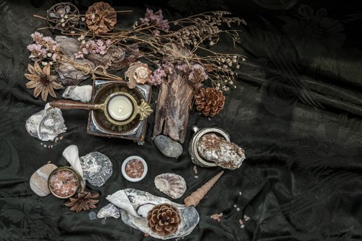 Beauty composition with Burning candle aroma oil lamp and Dry flower petals and Pine cones, Natural pine wood disc, Stones and Shells, Himalayan salt on dark background. Aromatherapy concept. Copy space.