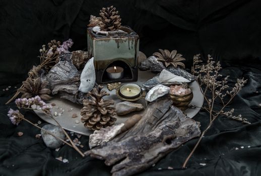 Beauty composition with Burning candle aroma oil lamp and Dry flower petals and Pine cones, Natural pine wood disc, Stones and Shells, Himalayan salt on dark background. Aromatherapy concept.