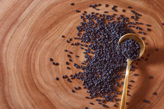 Black sesame with golden spoon lies on a wooden slice. Close-up. Macro effect photo. With copy space. High quality photo