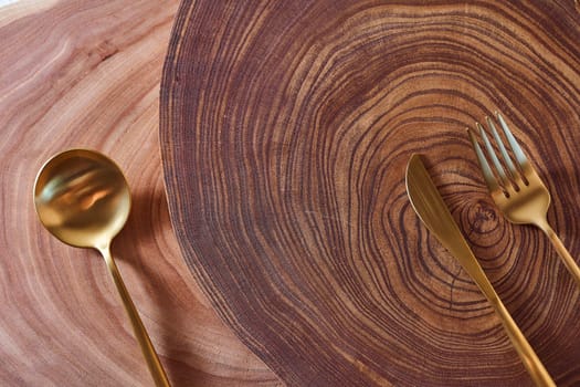 The golden spoon, knife and fork lies on a slice of a tree. wooden table. With copy space. High quality photo