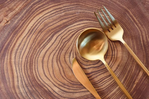 The golden knife, fork and spoon lies on a slice of a tree. wooden table. With copy space. High quality photo