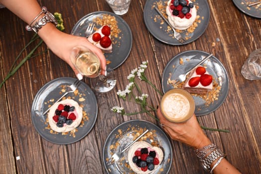 Bachelorette party, girls hands with drinks and sweet cakes with summer berries on a wooden table. Party, sweet table. Summer offer desserts in the restaurant