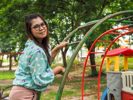 Portrait of Asian women wearing eyes Stand on an iron ladder in the park Wearing a green striped shirt Light purple pants And have a green tree background.