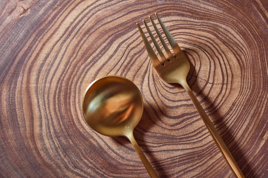 The golden fork and spoon lies on a slice of a tree. wooden table. High quality photo