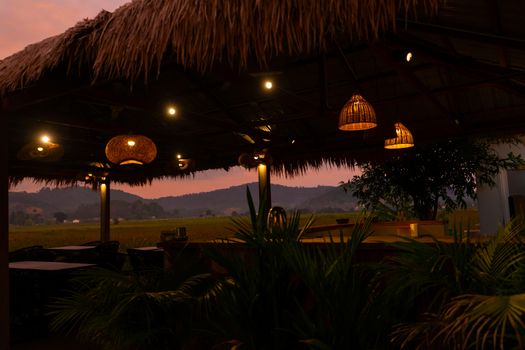 Beautiful pink sunset in the tropics. Street canopy from hay, kitchen area with rice field view.