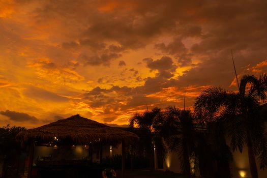 Beautiful orange fiery sunset in the tropics. Street canopy from hay, next to the pool and overlooking the rice field