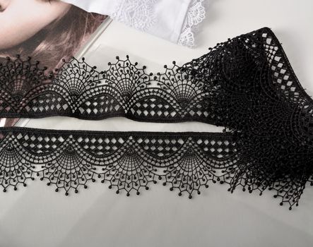 Tapes of black gentle guipure, beauty lace fabric on light background. Elastic material. Using for Atelier and needlework store.