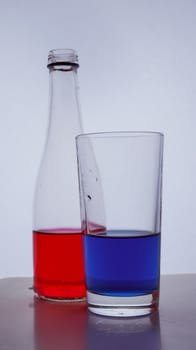 bottle and glass. In which the red and blue liquids are poured on a white background. Hight quality photo