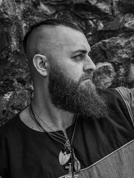 Viking warrior portrait with thick beard in front of a stone wall, black and white historical reenactment image