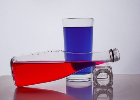 composition from a bottle and glasses with multicolored liquid on a white background. The bottle rests on a glass of whiskey. Hight quality photo