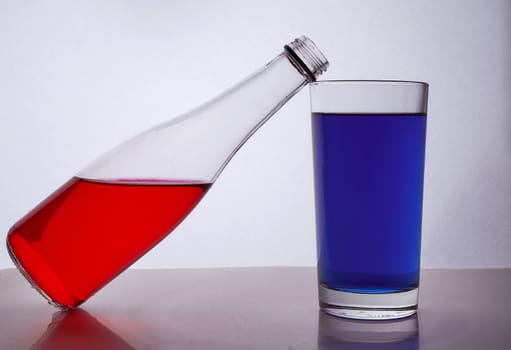 composition from a bottle and glasses with multicolored liquid on a white background. The bottle rests on a glass. Hight quality photo