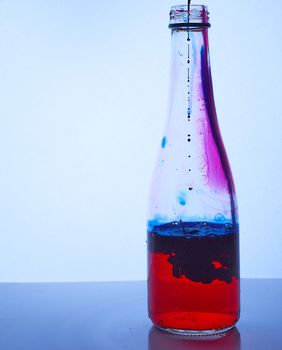 blue ink drips inside a glass bottle with red liquid. Mixing effect. Hight quality photo