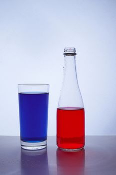 bottle and glass. In which the red and blue liquids are poured on a white background. Hight quality photo
