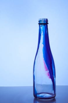 Glass bottle with blue red inside stands on a light background. Hight quality photo