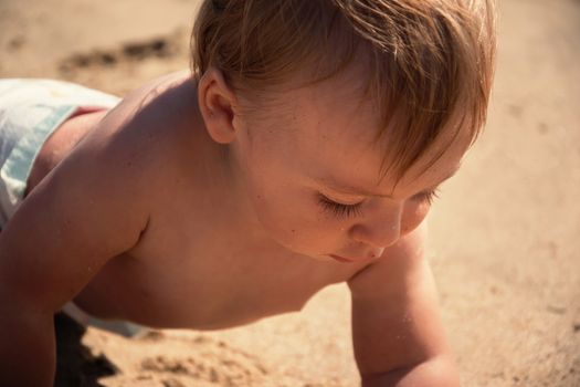 Baby boy discover sand at tropical beach close up. Curious toddler portrait who examining sand beach at summertime. Active caucasian little kid. Curiosity, concentration and discovering at holidays. 